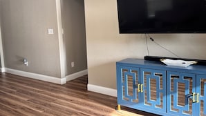 Una habitación con una televisión de pantalla plana montada en la pared, un aparador azul con cajones y suelo de madera.