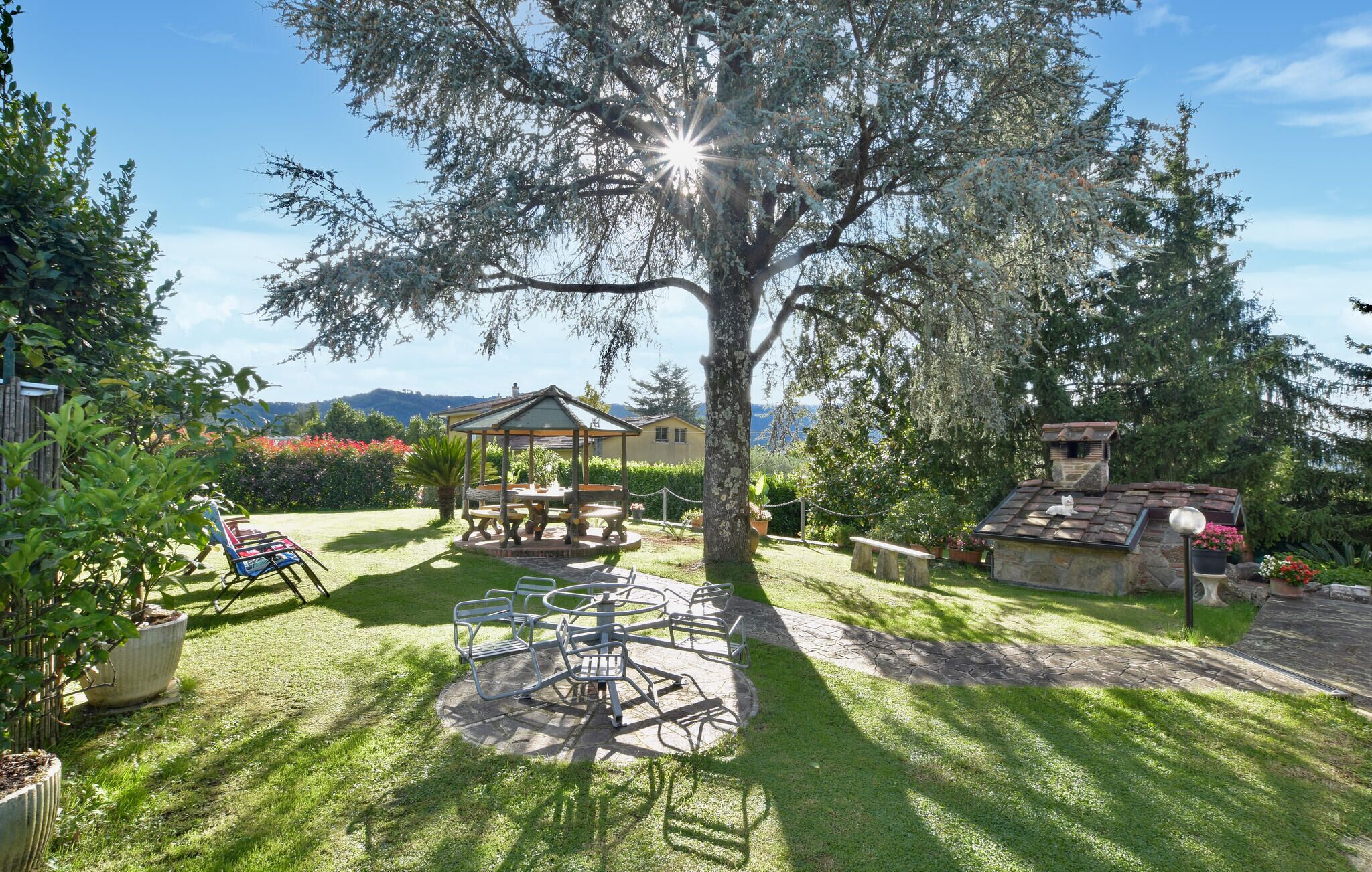 A gazebo with a table and chairs, surrounded by a well-maintained lawn and trees.