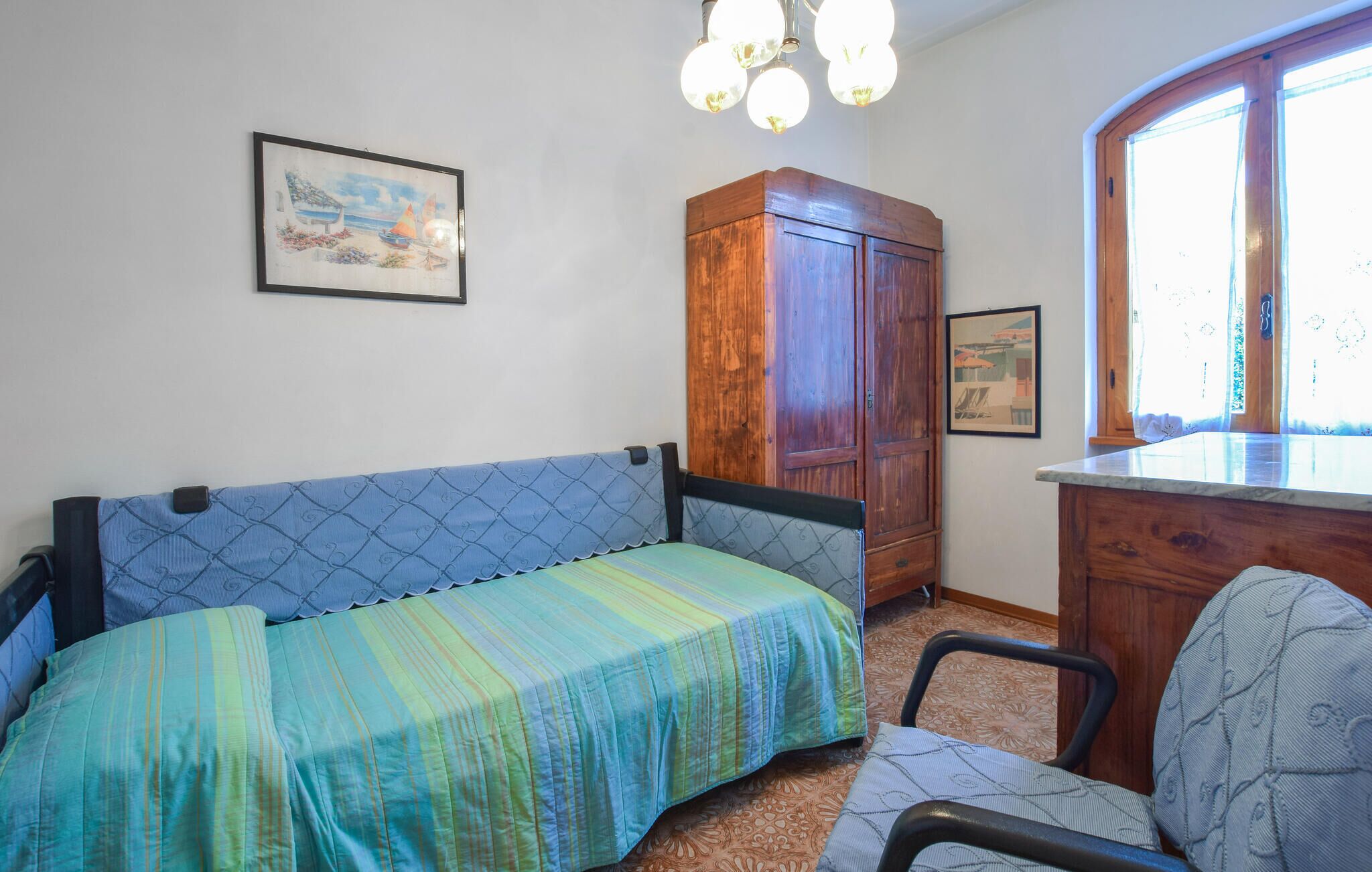 Une pièce comprenant un canapé-lit, une armoire en bois, une chaise et une fenêtre avec des rideaux.