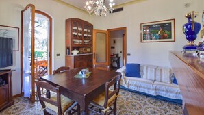 Un comedor con mesa y sillas de madera, una araña, un aparador con puertas de vidrio y un sofá con un diseño estampado.
