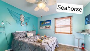A room with a bed, a ceiling fan, a window with blinds, a painting of a beach, and a shelf with items.