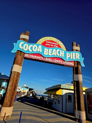 Une enseigne indiquant l’entrée de la jetée de Cocoa Beach, avec un message d’accueil et des mentions concernant les restaurants, les bars, les boutiques et la pêche.