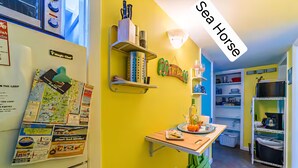 A kitchen with a yellow wall, a wooden table, and a shelf with kitchen utensils.
