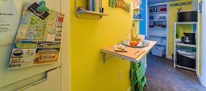 A kitchen with a yellow wall, a wooden table, and a shelf with kitchen utensils.