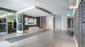 Una hall d'albergo moderna con una reception, una porta in vetro che conduce a una palestra e una telecamera di sicurezza a soffitto.