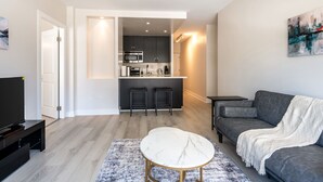 Un soggiorno moderno con un divano grigio, un tavolino bianco e una cucina sullo sfondo.
