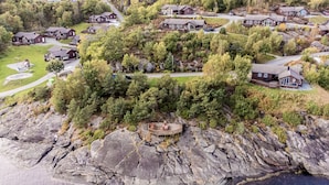 An aerial view of a coastal residential area with multiple houses, a rocky shoreline, and a small wooden deck overlooking the water.