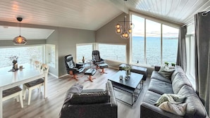 A spacious living area with a large window overlooking the sea, a dining table, and comfortable seating.
