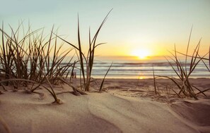 A beach scene with sand and grass in the foreground and a sunset over the ocean in the background. - Lovely home in Sianozety with sauna (Sianozety)