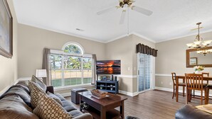 A spacious living room with a large window, a flat-screen TV, a dining area with a chandelier, and a ceiling fan. - Escape to Comfort at Magnolia Place | MP 4661-102 (Myrtle Beach)