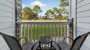 A porch with two chairs and a table, overlooking a grassy area with trees. - Escape to Comfort at Magnolia Place | MP 4661-102 (Myrtle Beach)
