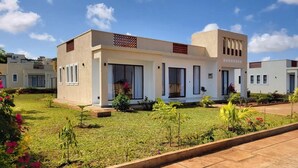 A modern two-story house with a flat roof, large windows, and a well-maintained lawn. - Charming 2-bedroom bungalow in Kilifi County with AC (Kilifi County)