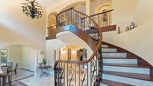 Una imponente escalera de caracol con barandillas metálicas ornamentales y escalones de madera, que conduce a un piso superior.