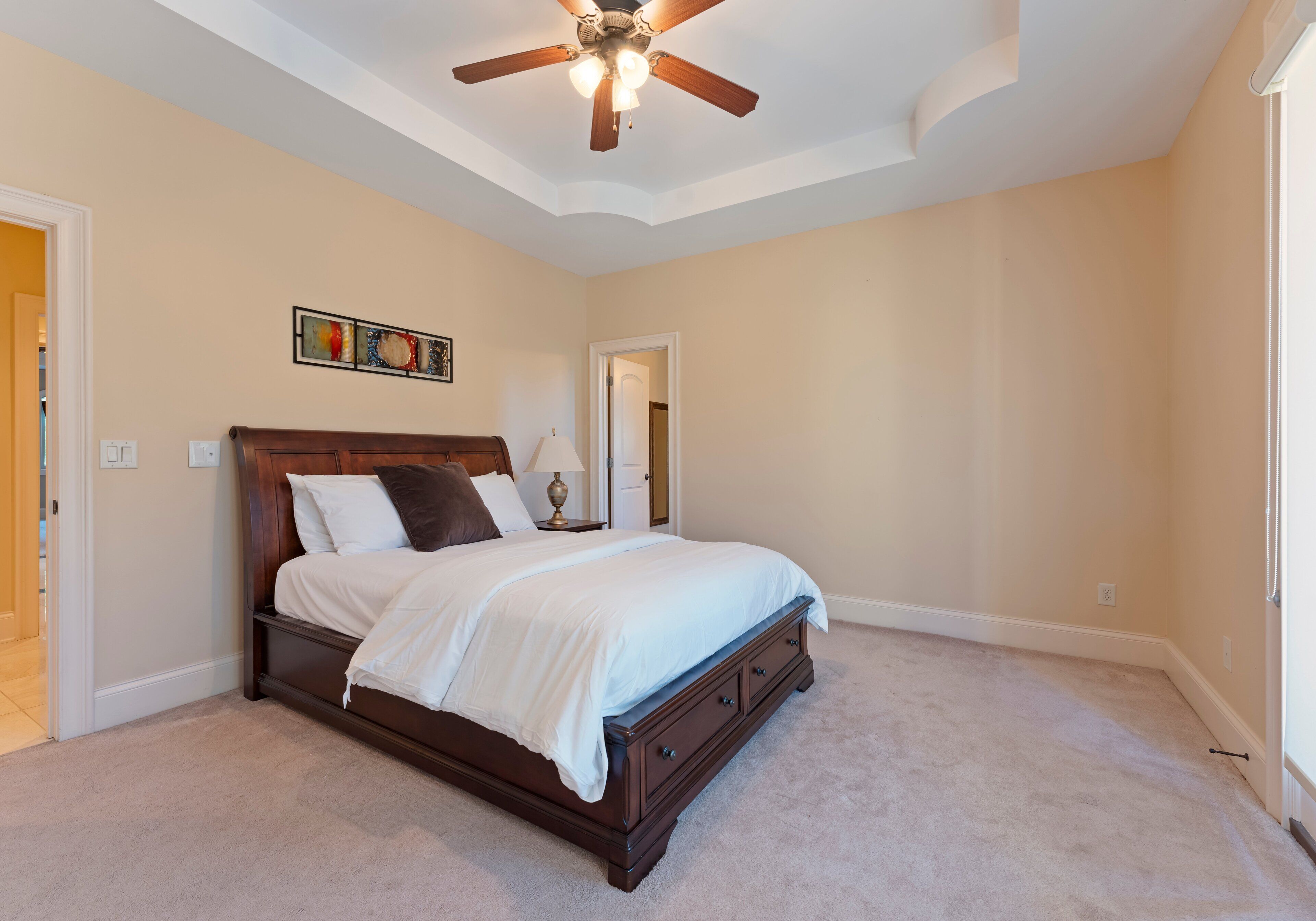 A bedroom with a large bed, a ceiling fan, and a door leading to another room.