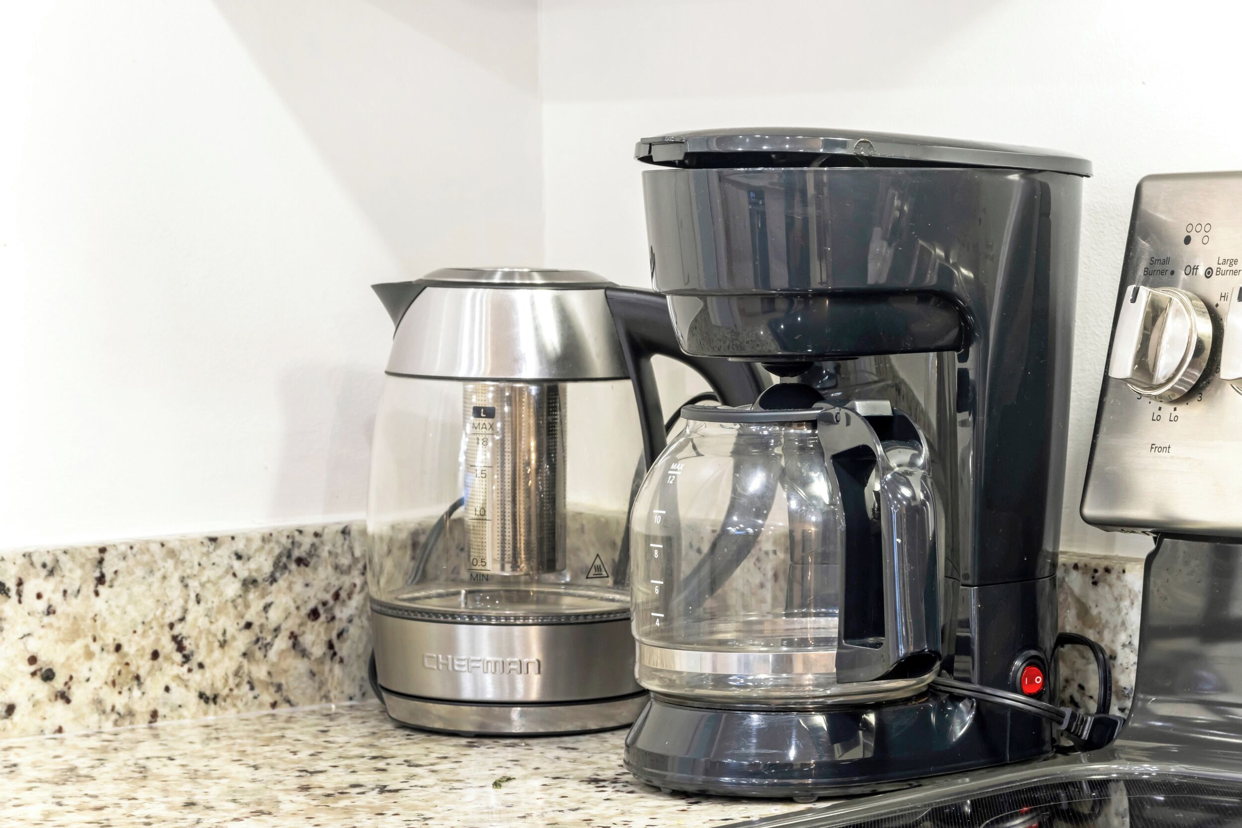 A coffee maker with a clear carafe and a small container on a granite countertop.