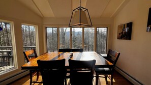 A dining area with a large wooden table, black chairs, and a hanging light fixture.