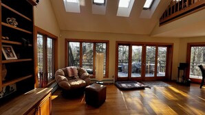 A spacious living room with a large window, a cushioned chair, a small ottoman, and a treadmill. - THE BIJOU -  a Precious Gem in the Green Mountains. HOT TUB, PET OK, HANDICAP (Rochester)