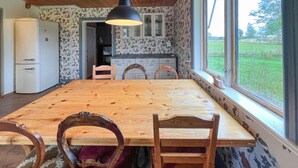 A dining area with a wooden table and chairs, a hanging light fixture, a refrigerator, and a view of the outdoors through large windows. - Lovely home in Furudal with sauna (Furudal)