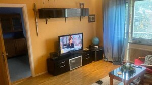 A living room with a TV on a black stand, wooden flooring, a globe on a side table, and a window with curtains. - Apartment in S West Sthlm close to Metro (Hägersten)