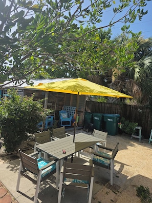 Eine Terrasse im Freien mit Tisch und Stühlen, einem gelben Sonnenschirm und einem Holzzaun.