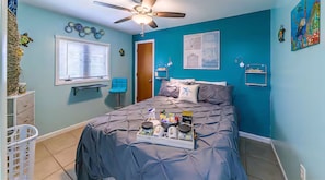 Een kamer met een bed, een plafondventilator, een raam met jaloezieën, een deur en een muur met een schilderij.
