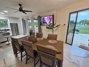 Un espace repas moderne avec un sol en marbre, un ventilateur de plafond, un téléviseur à écran plat et une vue sur l’extérieur.