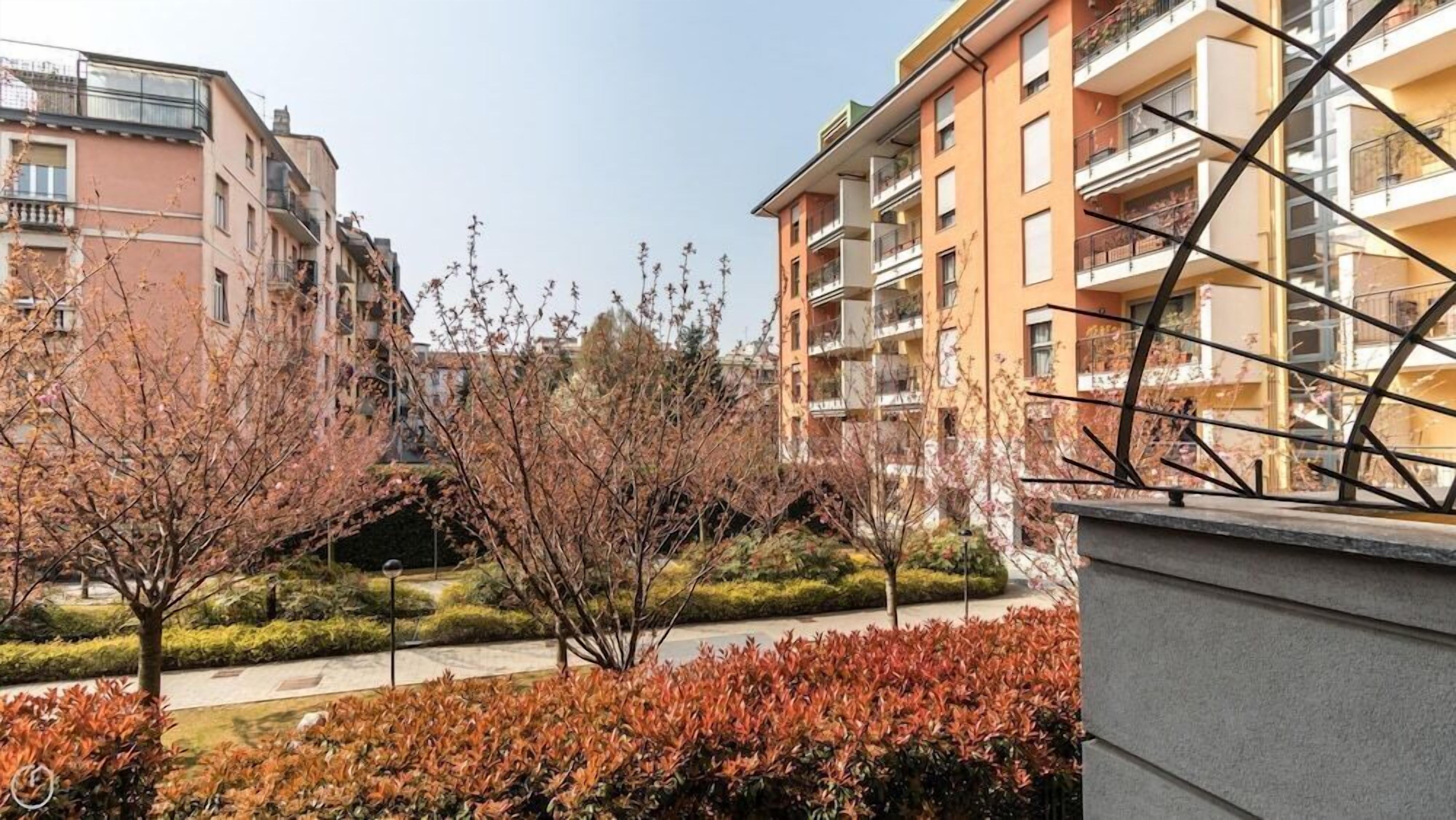 Ein Wohngebäude mit Balkonen und einem Gartenbereich mit Sträuchern, bewölkter Himmel.