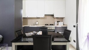 A modern kitchen with white cabinets, a black dining table with two chairs, and a coffee maker on the counter. - Italianway - Marcantonio (Milan)