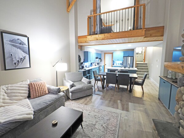 A spacious living area with a high ceiling, a dining area, and a kitchen with blue cabinets.