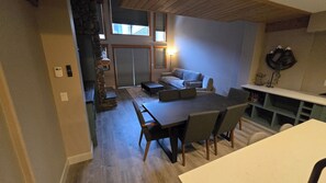 Ein modernes Wohnzimmer mit einer Wand aus Stein, einer Couch, einem Esstisch mit Stühlen und einer Küchenzeile mit Arbeitsfläche und Regalen.
