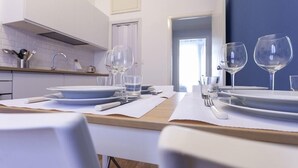A modern kitchen with white cabinets, a wooden countertop, and a dining area set with white plates, glasses, and cutlery. - Italianway Corso Lodi 121 (Milan)