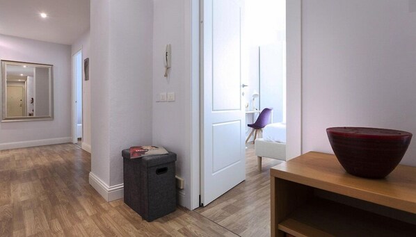 Une chambre d’hôtel avec un plancher en bois, une porte, une petite poubelle, un bol rouge posé sur une table en bois, et une chaise à l’arrière-plan.