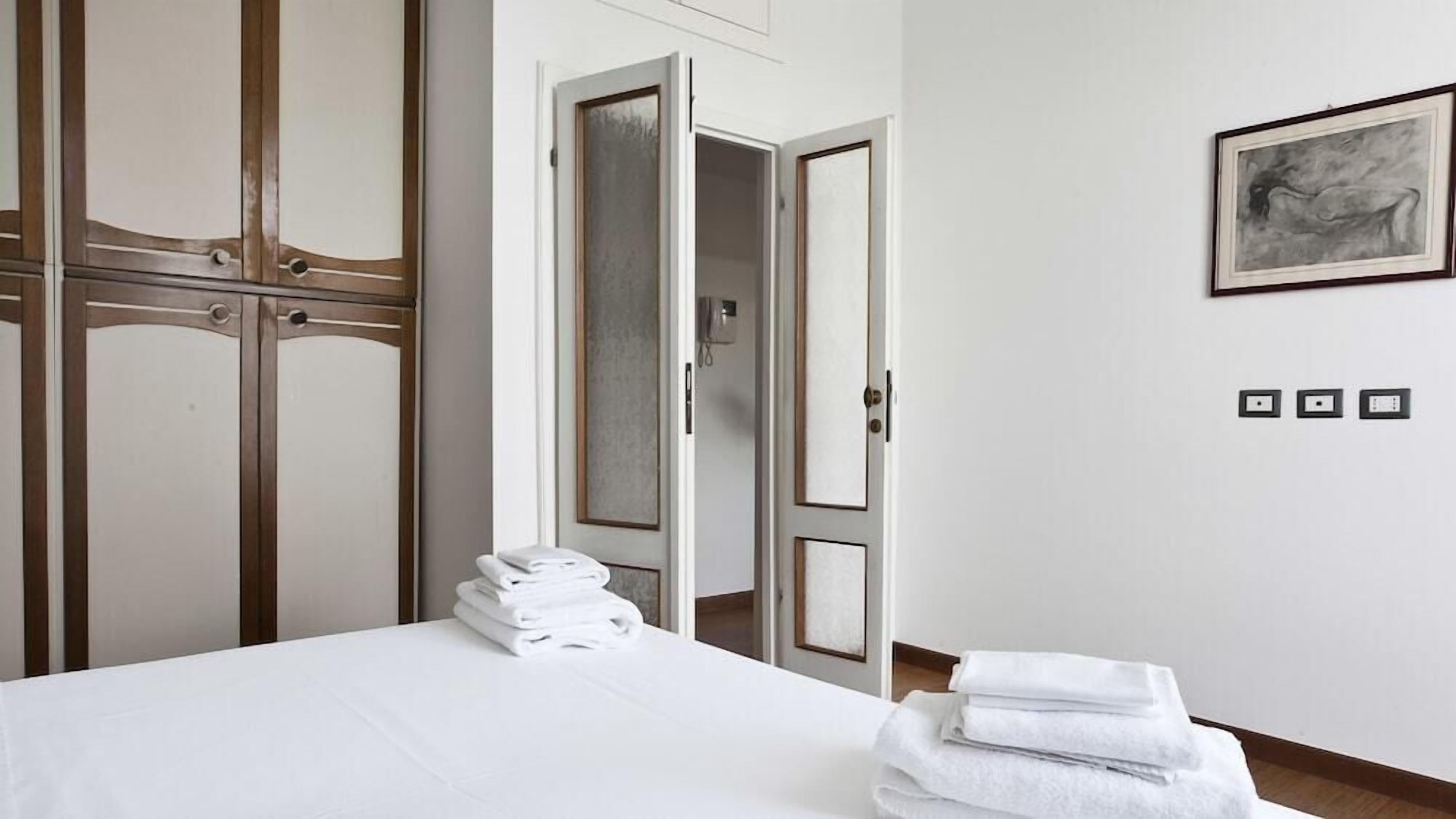 Habitación de hotel con cama, una pila de toallas, un armario y un cuadro en la pared.