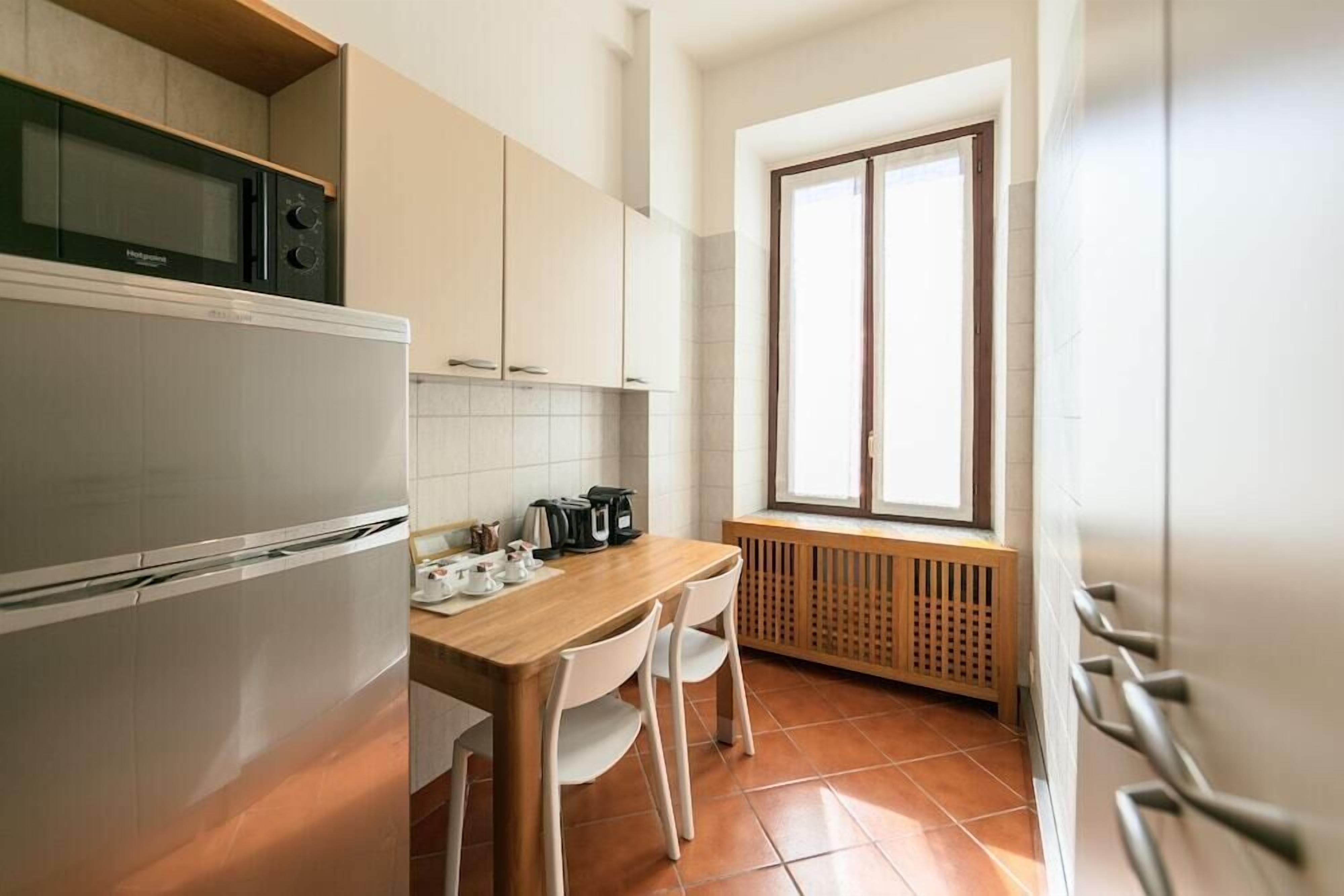 Eine kleine Küche mit Kühlschrank, Mikrowelle und einem Holztisch mit Stühlen.