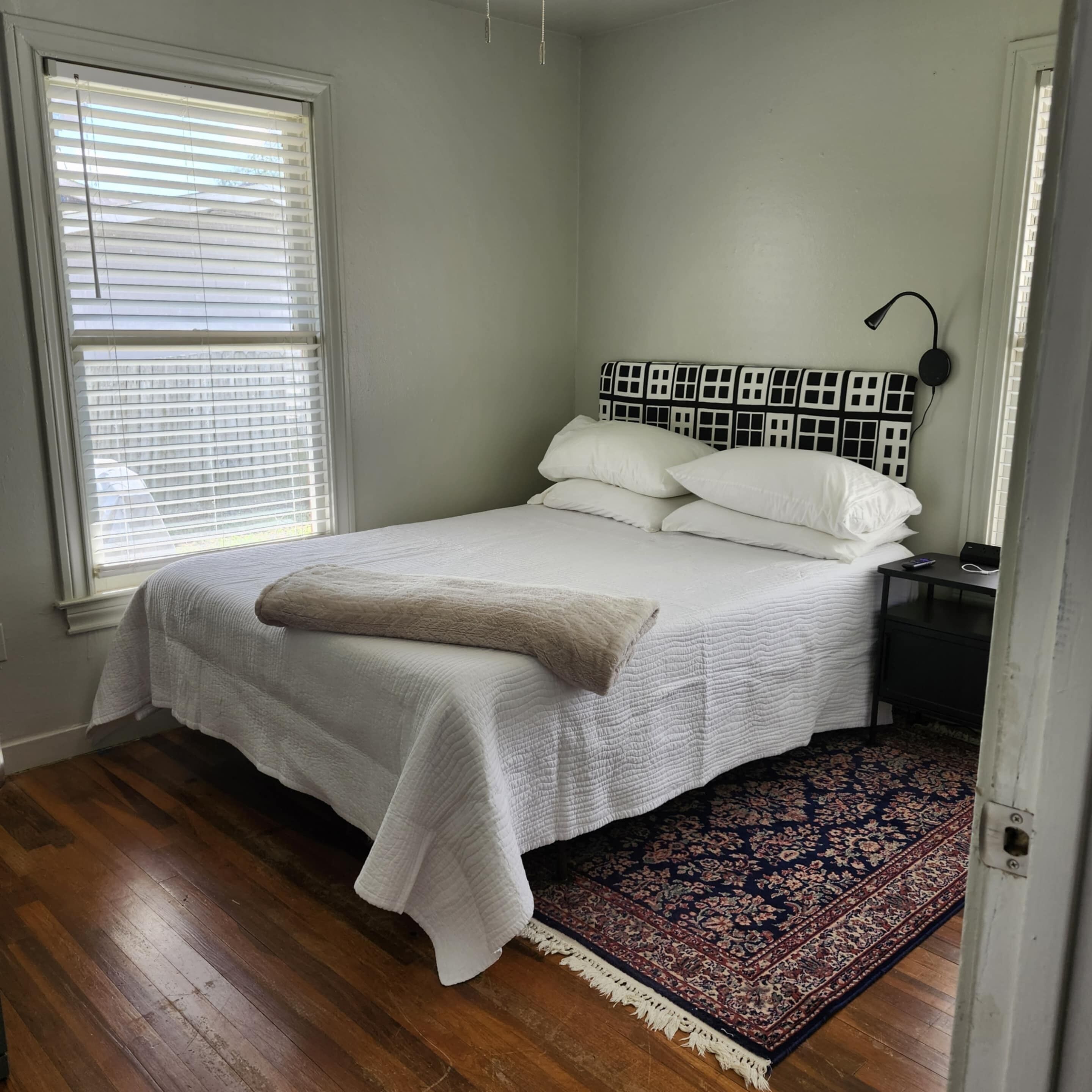Un dormitorio con cama, mesita de noche, lámpara y ventana con persianas.