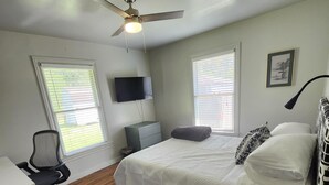 A bedroom with a bed, a desk, a chair, a TV, and a ceiling fan.