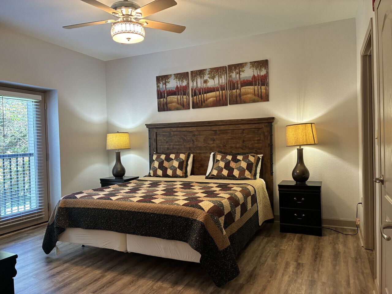 A bedroom with a wooden bed, two bedside tables with lamps, a ceiling fan, and a window with blinds.