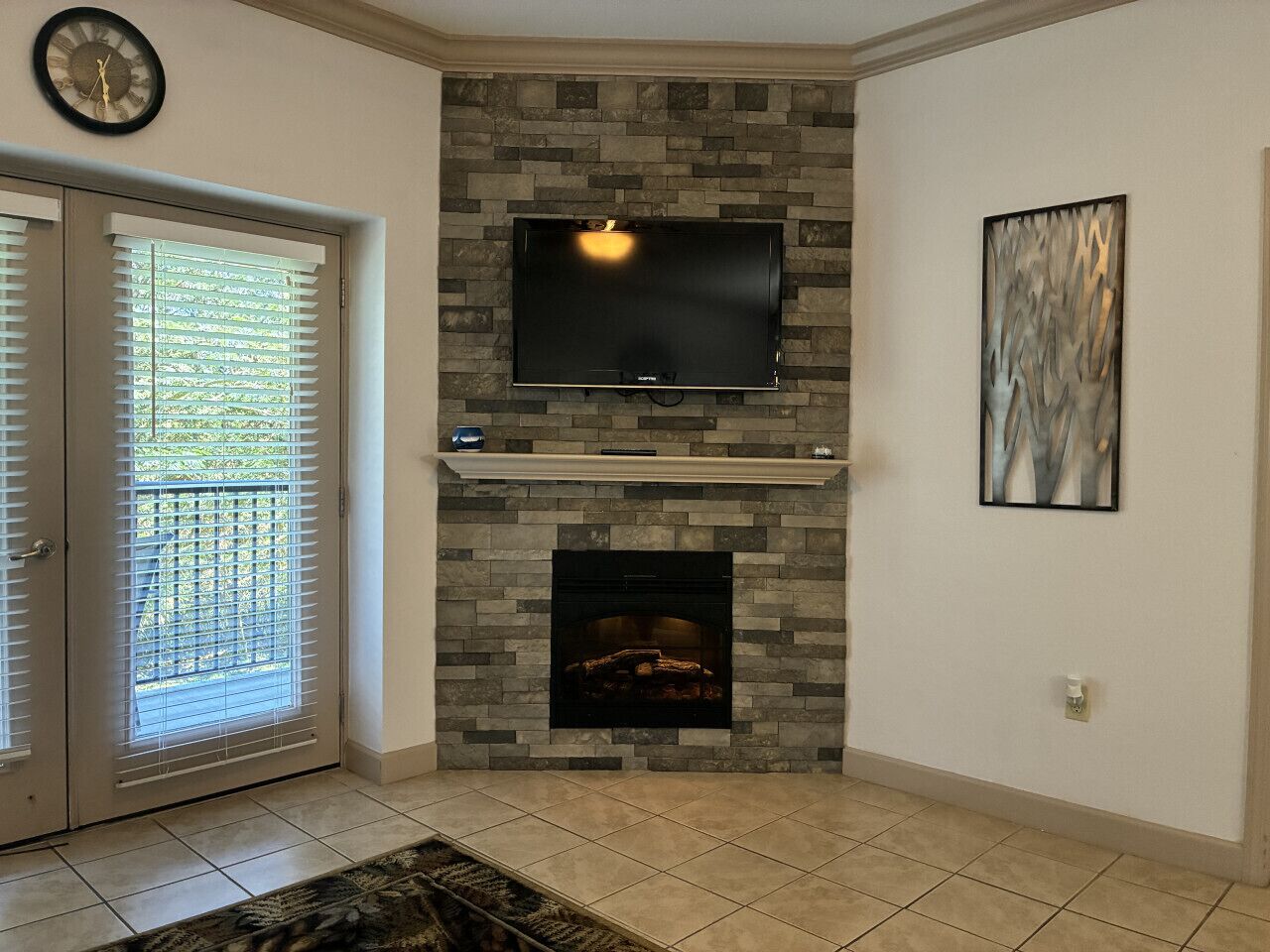 A living room with a stone fireplace, a mounted flat-screen TV, and a framed abstract artwork on the wall.