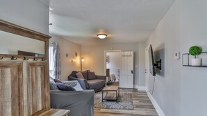 A living room with a sofa, a coffee table, and a TV mounted on the wall. - Gowen 2411 - 3BR Mid-Term Stay, All Utilities Incl (Wausau)