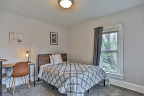 A bedroom with a bed, a desk, a chair, a window with curtains, and two wall-mounted pictures.