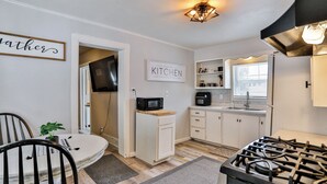 A compact kitchen with white cabinets, a gas stove, a microwave, and a coffee maker. There is a dining table with chairs and a potted plant. - Gowen 2415 - 2BR Mid-Term Stay, All Utilities Incl (Wausau)