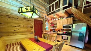 L’intérieur d’un chalet en bois comprend une table à manger, des bancs, un coin cuisine équipé d’appareils électroménagers et un luminaire suspendu.