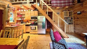 L’intérieur d’un chalet en bois comprend une cuisine, un coin repas et une chambre à l’étage, accessible par un escalier.