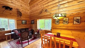 L’intérieur d’une cabane en rondins comprend un coin repas, un ensemble de canapés et une cheminée.