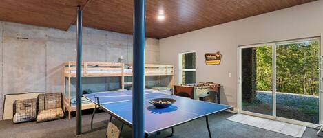 Una habitación con literas, mesa de futbolín y mesa de ping pong.