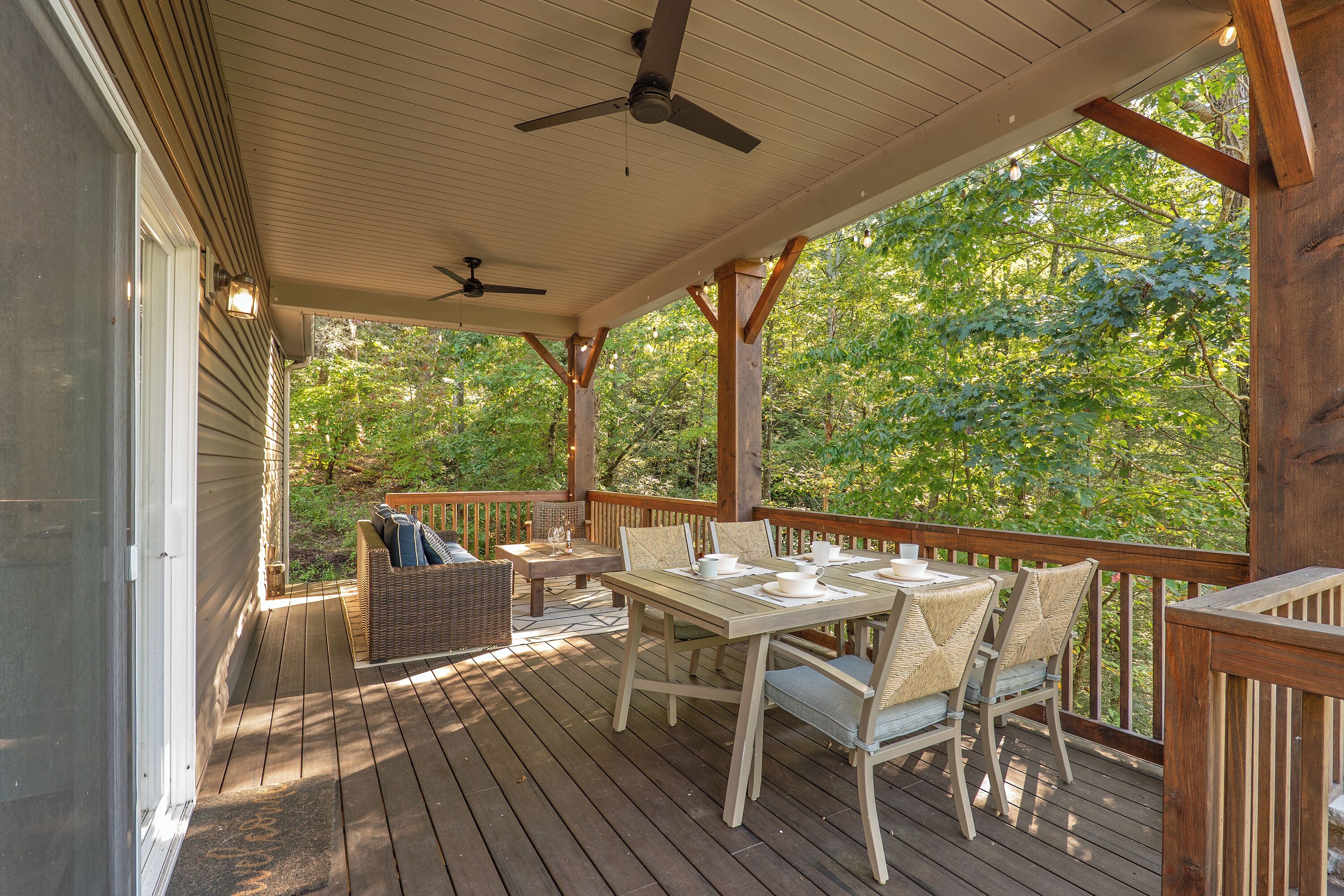 A covered deck with a table and chairs, a ceiling fan, and a view of trees.