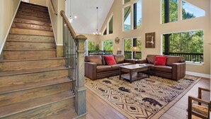 Ein geräumiger Wohnbereich mit einer Holztreppe, einem großen Ecksofa und einem gemusterten Teppich.