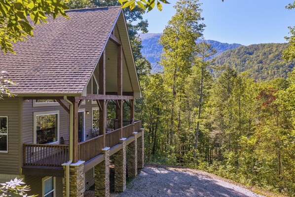 A cabin with a balcony overlooking a forested area and mountains in the background.