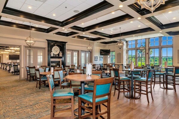 A spacious dining area with multiple tables and chairs, a fireplace, and large windows offering a view of the outdoors.