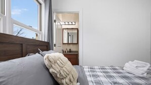 A bedroom with a bed, a bedside table, a mirror, and a window.